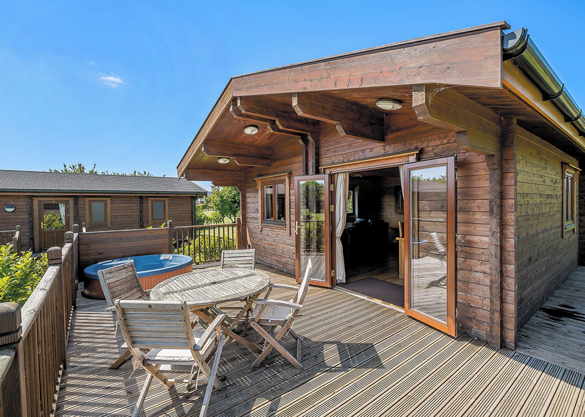 A wooden cabin with a deck, a hot tub, and a glass door entrance.