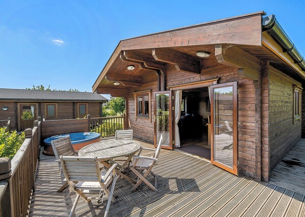 Une cabane en bois dotée d’une terrasse, d’un bain à remous et d’une entrée avec une porte en verre.