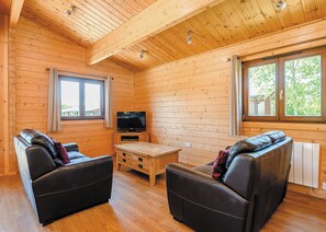 L’intérieur d’un chalet en bois est aménagé avec deux canapés en cuir, une table basse en bois, un téléviseur et de grandes fenêtres.