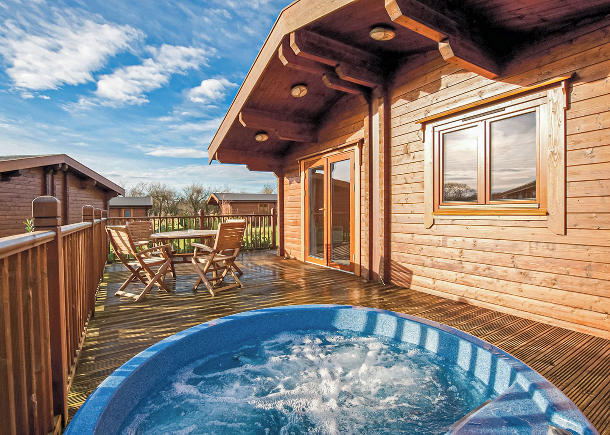 A wooden deck with a hot tub, outdoor furniture, and a view of the surrounding area.