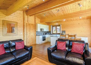 Ein Innenraum einer Holzhütte, mit einer Küchenzeile und zwei Ledersofas mit roten Kissen.