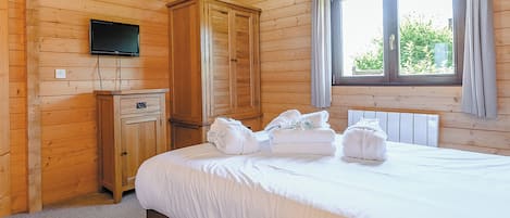 A wooden-paneled room with a bed, a television mounted on the wall, and a window with curtains.