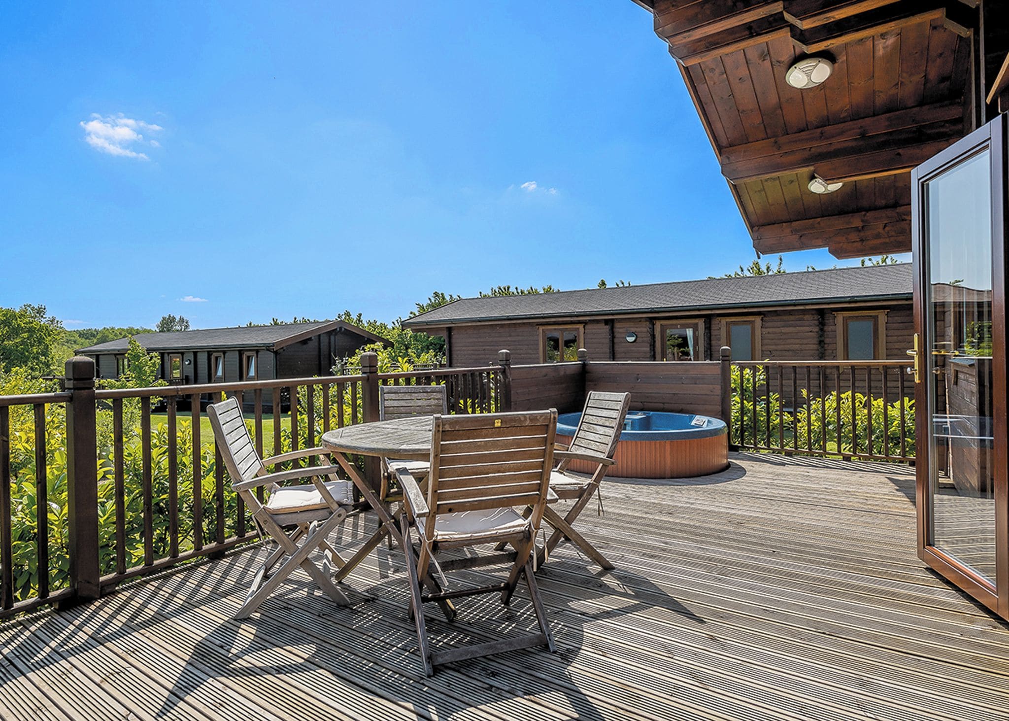 En træterrasse med et bord og stole, et boblebad og udsigt til et hus i baggrunden.