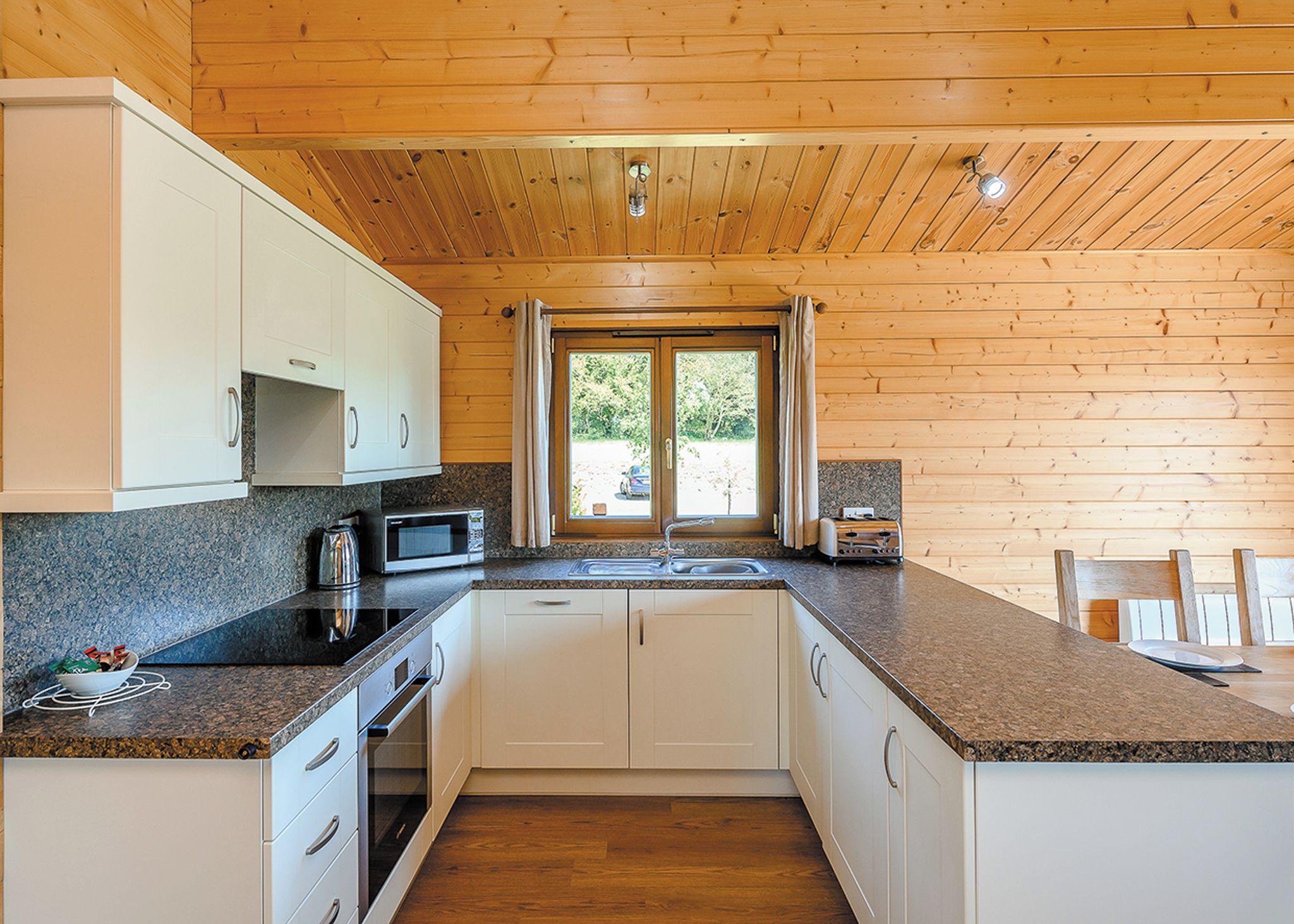 A compact kitchen with white cabinets, a granite countertop, a microwave, and a sink.