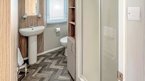 Un baño con tocador de madera, lavamanos, inodoro y zona de ducha.