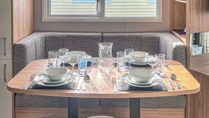 Una zona de comedor con una mesa preparada para dos, un banco y una ventana con persianas.