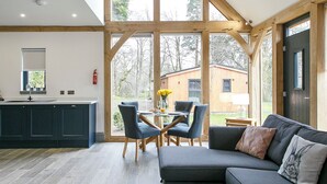 Una cocina moderna con armarios oscuros, un comedor con mesa y sillas de vidrio, y un ventanal con vistas al exterior.