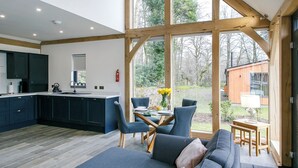 Una cocina moderna con armarios oscuros, una zona de comedor con sillas azules y un amplio ventanal con vistas a un jardín.