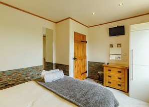 A bedroom with a bed, a wooden wardrobe, a small stool, and a television mounted on the wall.
