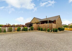 A building with a sloped roof, a wooden fence, and a gravel driveway.