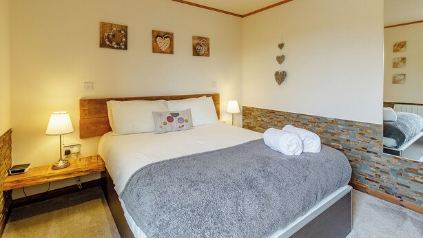 Quarto de hotel com cama, duas luminárias de cabeceira, encosto de madeira e arte decorativa na parede.