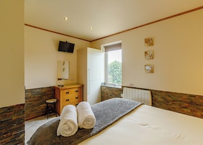 A hotel room with a bed, a wooden dresser, a television, a window with a view, and a radiator. - Luxurious and stylish modern lodge with one master double and one twin. (Haswell, Nr Durham)