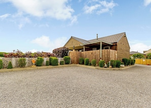 A building with a sloped roof, a wooden fence, and a gravel driveway. - Luxurious and stylish modern lodge with one master double and one twin. (Haswell, Nr Durham)