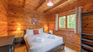 Een houten slaapkamer met een bed, twee bedlampen, een raam met gordijnen en een schilderij aan de wand.