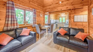 Een chalet met houten wanden, een eethoek, twee zwarte leren banken met oranje kussens, en een keuken op de achtergrond.