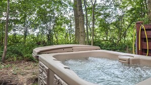 Een hottub in een bebost gebied met een stenen muur en een houten terras.
