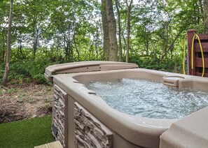 Un bain  à remous situé dans un espace boisé, avec un mur en pierre et une terrasse en bois.