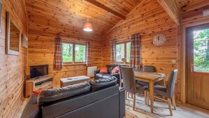 A wooden cabin interior with a sofa, TV, dining table, chairs, and plaid curtains. - Woodland Willow Lodge (Ellesmere)