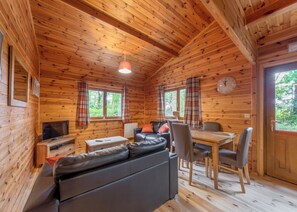 A wooden cabin interior with a sofa, TV, dining table, chairs, and plaid curtains. - Woodland Willow Lodge (Ellesmere)