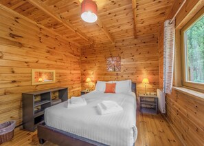 Une chambre à coucher dans un chalet en bois, avec un lit, deux tables de chevet, des lampes, une fenêtre et un tableau accroché au mur.