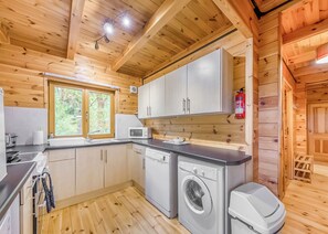 Interior de una cabaña de madera con cocina que incluye microondas, lavamanos y lavadora.