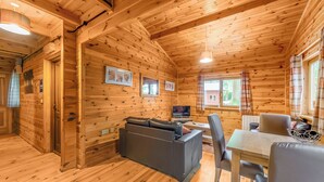 A wooden cabin interior with a sofa, a table, chairs, a television, and framed pictures on the walls. - Woodland Willow Lodge (Ellesmere)