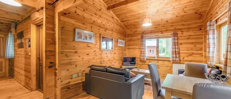 L’intérieur d’un chalet en bois, avec un canapé, une table, des chaises, un téléviseur et des tableaux encadrés accrochés aux murs.