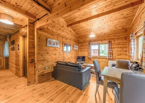 L’intérieur d’un chalet en bois, avec un canapé, une table, des chaises, un téléviseur et des tableaux encadrés accrochés aux murs.