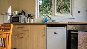 A compact kitchen with wooden cabinets, a white refrigerator, a microwave, and an oven. - 2 bedroom accommodation in Ruthernbridge, Nr Bodmin (Ruthernbridge, Nr Bodmin)