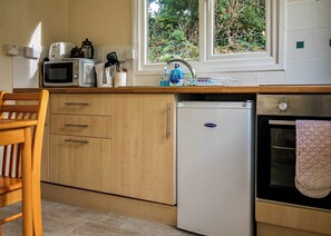 Une cuisine de taille réduite, dotée de meubles en bois, d’un réfrigérateur blanc, d’un four à micro-ondes et d’un four traditionnel.