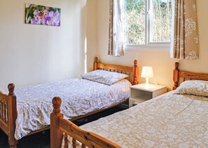 Une chambre à coucher avec deux lits en bois, une table de chevet avec une lampe, une fenêtre avec des rideaux et un tableau accroché au mur.