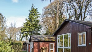 A row of wooden cabins with large windows, surrounded by a well-maintained lawn and trees. - 2 bedroom accommodation in Ruthernbridge, Nr Bodmin (Ruthernbridge, Nr Bodmin)