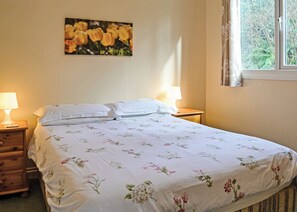 Une chambre à coucher comprenant un lit, deux tables de chevet, une commode, une fenêtre avec des rideaux et un tableau floral accroché au mur.