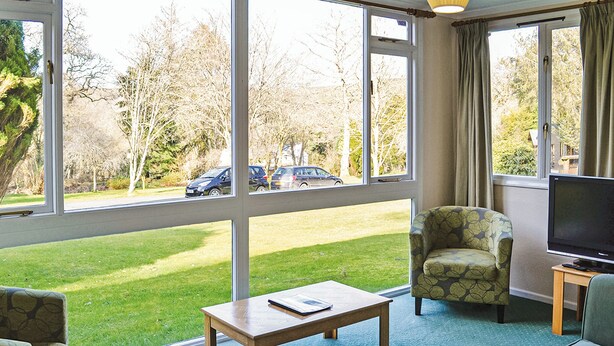 A room with a large window, a television, a sofa, and a table. - 2 bedroom accommodation in Ruthernbridge, Nr Bodmin (Ruthernbridge, Nr Bodmin)