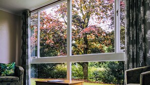 A room with a large window, a wooden table, and two patterned armchairs. - 2 bedroom accommodation in Ruthernbridge, Nr Bodmin (Ruthernbridge, Nr Bodmin)