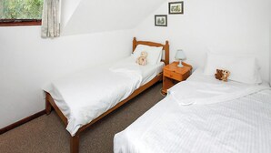 Une chambre avec deux lits simples, une table de chevet avec une lampe et un ours en peluche sur l’un des lits.