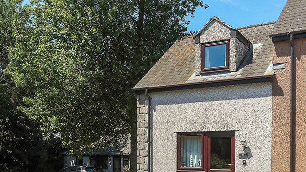 Une maison à deux étages avec un petit porche, une fenêtre avec des rideaux et une porte.