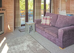 A room with a purple sofa, a small wooden table, and a view of a wooden deck outside.