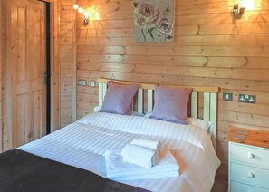 A wooden-paneled room with a bed, two pillows, a painting, and wall-mounted lights. - 2 bedroom accommodation in Easingwold (Easingwold)