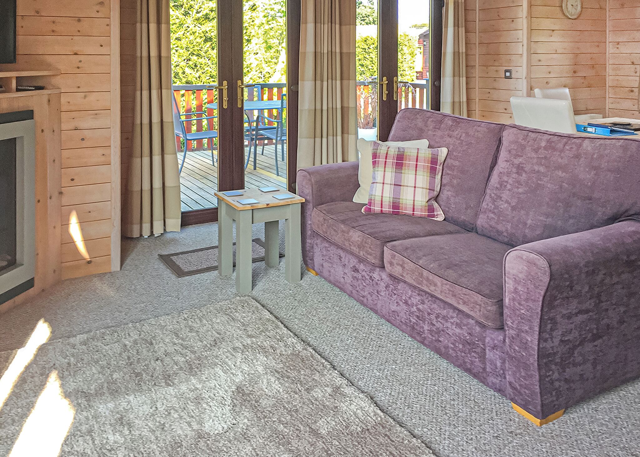 A room with a purple sofa, a small wooden table, and a view of a wooden deck outside.