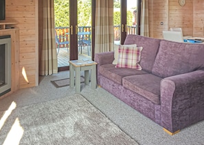 A room with a purple sofa, a small wooden table, and a view of a wooden deck outside. - 2 bedroom accommodation in Easingwold (Easingwold)