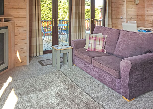 A room with a purple sofa, a small wooden table, and a view of a wooden deck outside. - 2 bedroom accommodation in Easingwold (Easingwold)