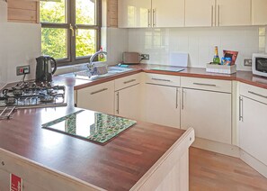 A kitchen with a gas stove, a kettle, a microwave, and a window with a view of trees.
