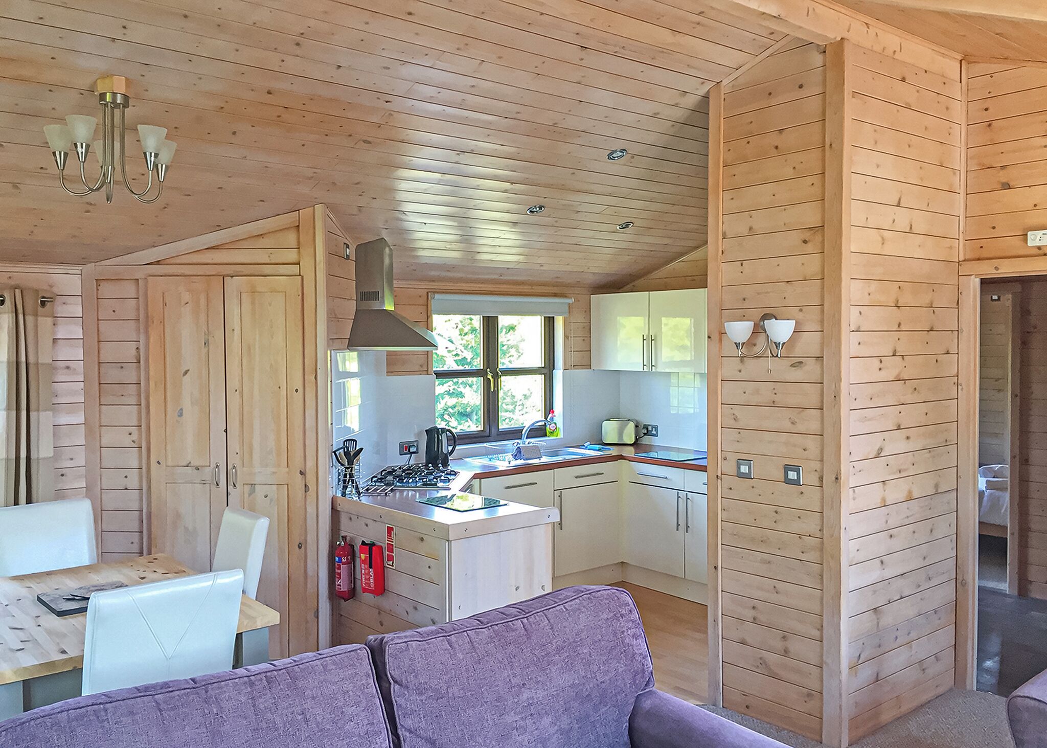 A wooden cabin interior with a dining area, kitchen, and a purple sofa.