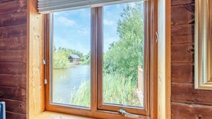 A wooden cabin with a window overlooking a river and greenery. - Superb lodge perched on the lake, perfect for romantic breaks. (Anglesey)