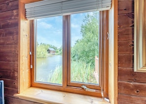 A wooden cabin with a window overlooking a river and greenery.