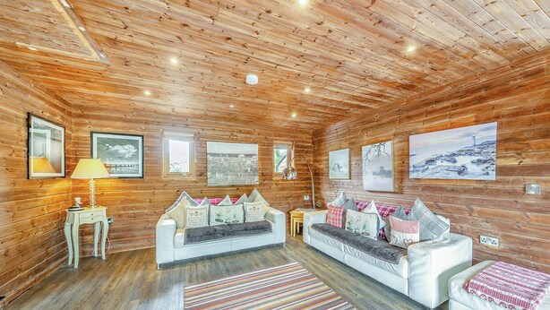 A log cabin interior with a white sofa, a lamp, and framed pictures on the walls. - Superb lodge perched on the lake, perfect for romantic breaks. (Anglesey)