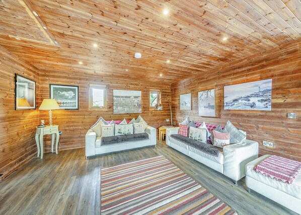 A log cabin interior with a white sofa, a lamp, and framed pictures on the walls.
