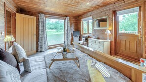 A log cabin interior with a sofa, a dining table, a TV, and a view of a lake. - Superb lodge perched on the lake, perfect for romantic breaks. (Anglesey)