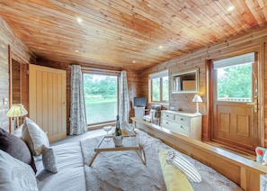 A log cabin interior with a sofa, a dining table, a TV, and a view of a lake.